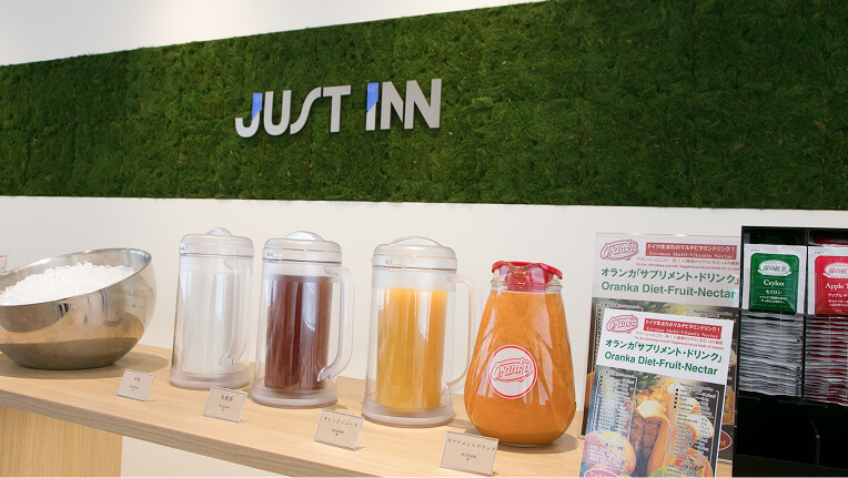 JUST INNのロゴ壁面前に並ぶコーヒーやジュースなどのドリンクバー